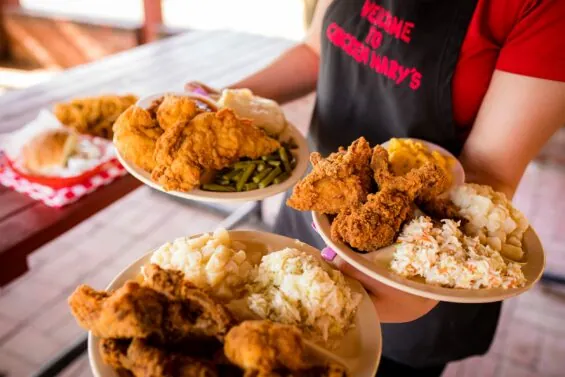 Server at Chicken Mary's holding three plates of fried chicken, cole slaw and mashed potatos.