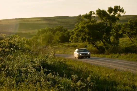 Car rounding the corner on a beautiful dirt road surrounded by rolling, green hills at sunset.