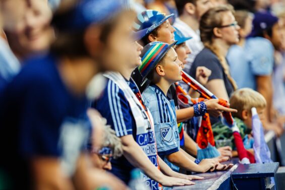 Close-up of front-row fans at a Sporting KC game wearing the team's jerseys intensely watching the game.